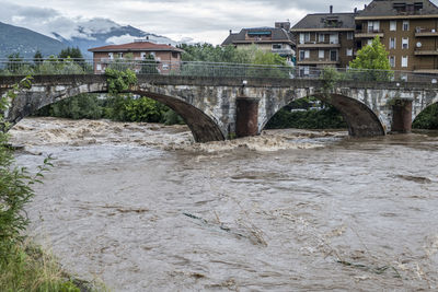 Arch bridge over river amidst buildings against sky