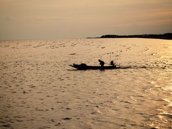 Silhouette people on shore against sky during sunset