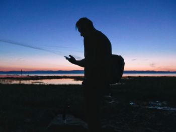 Silhouette man photographing on mobile phone against sky during sunset