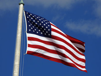 Low angle view of american flag waving against blue sky