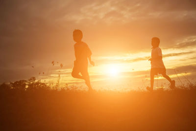 Silhouette friends on beach against sky during sunset