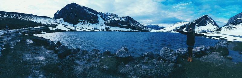 Panoramic view of excited woman standing on rock formation by lake against sky