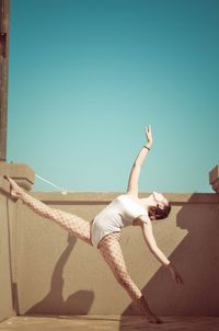 Ballet dancer dancing on building terrace against clear blue sky during sunny day