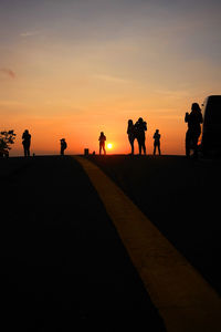 Silhouette people standing on road against orange sky