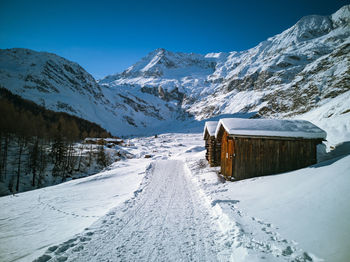 Snow covered huts by mountains in a winter scene against sky