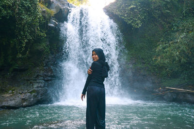 Full length of young woman standing in waterfall