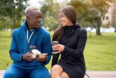 Smiling couple with food sitting on bench at park