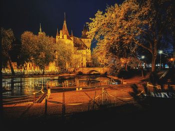 Illuminated building by river against sky at night