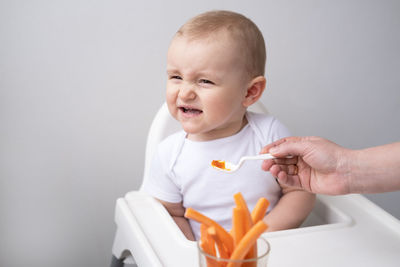 Hand of woman with spoon feeding baby at home