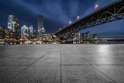 Illuminated bridge by buildings against sky in city