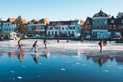 Group of people skating on a frozen river in city by buildings against sky