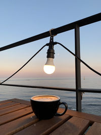 Coffee cup on table by sea against clear sky