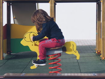 Side view of girl sitting on play equipment