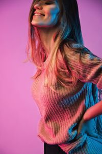 Close-up of young woman standing against pink background