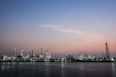 Illuminated factory by river against sky