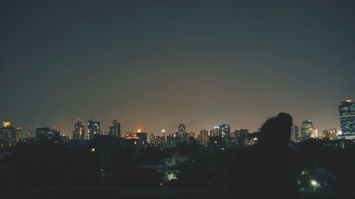 Rear view of illuminated cityscape against sky at night