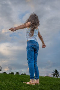 Rear view of woman standing on grassy field against sky