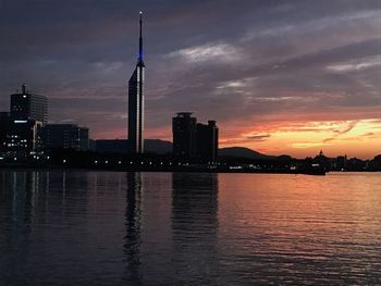 Buildings by river against sky during sunset