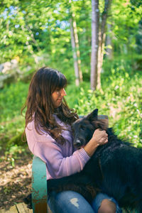 Young latina woman hugging her dog while sitting on a vintage turquoise chair outside her home.