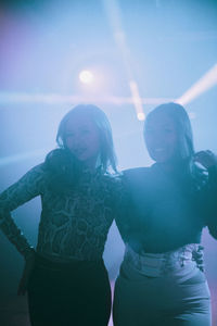 Portrait of happy young women standing with arms around at nightclub