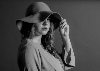 Portrait of young woman wearing hat against gray background