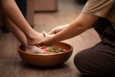 Woman feet dipped in water with petals in a wooden bowl.