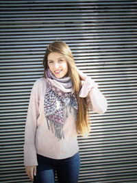 Portrait of smiling young woman with long blond hair against blinds