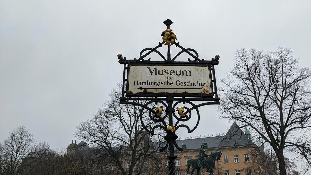 bare tree, architecture, tree, sky, built structure, text, communication, low angle view, building exterior, nature, sign, no people, lighting, western script, plant, day, outdoors, guidance, building, history, light fixture, the past, city, travel destinations