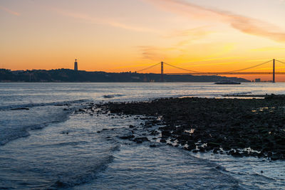 Suspension bridge over sea against sky during sunset