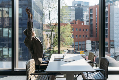 Businessman stretching arms sitting at desk by window in office