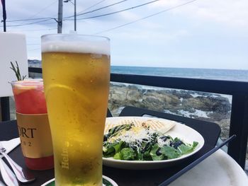 Close-up of beer on table by sea against sky