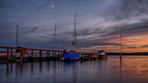 Sailboats moored in sea at sunset