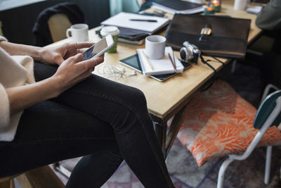 Midsection of businesswoman using smart phone at table in creative office