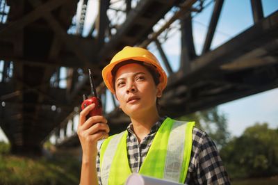 Engineer woman in hard hat holding walkie talkie while standing at construction site.