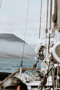 Sailing ship moving on sea by mountains against sky