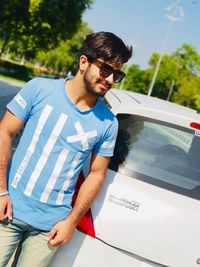 Young man looking away while standing on car