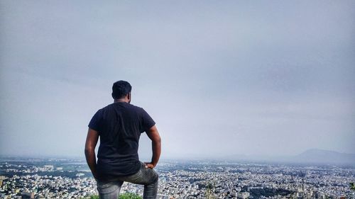 Rear view of man standing on sea against cityscape