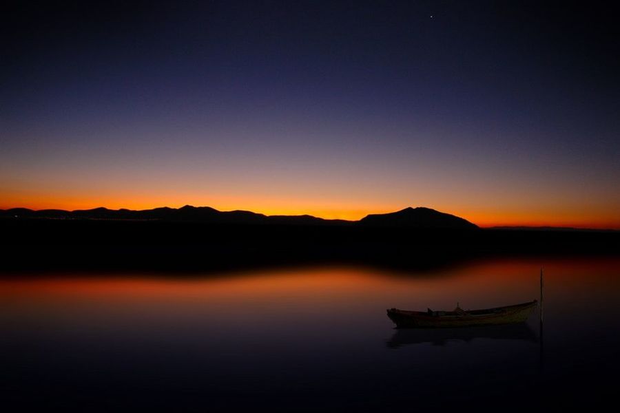 sunset, water, tranquil scene, silhouette, scenics, tranquility, copy space, beauty in nature, mountain, lake, clear sky, orange color, reflection, nature, idyllic, mountain range, dusk, calm, nautical vessel, waterfront