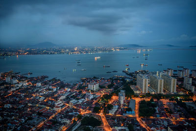 Aerial view of illuminated city by sea against sky