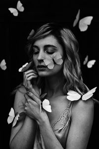 Close-up of young woman with butterflies against black background