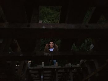 Portrait of woman peeking through broken wooden bridge