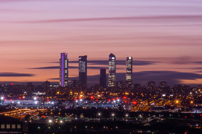 Illuminated modern buildings in city against sky at sunset