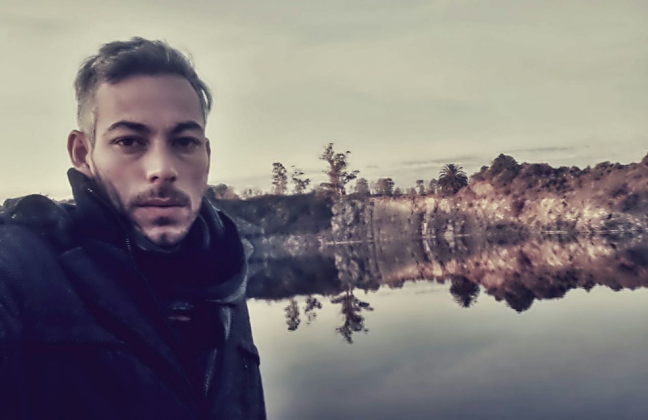 lifestyles, reflection, sky, leisure activity, water, lake, person, headshot, nature, portrait, looking at camera, tranquility, scenics, tree, young adult, casual clothing, cloud - sky, tranquil scene