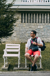Man sitting with backpack on white wooden chair against building