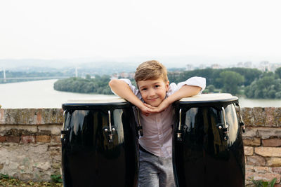 Portrait of boy leaning on bongo against clear sky