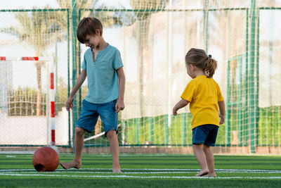 Boy and girl playing football on green sports field.