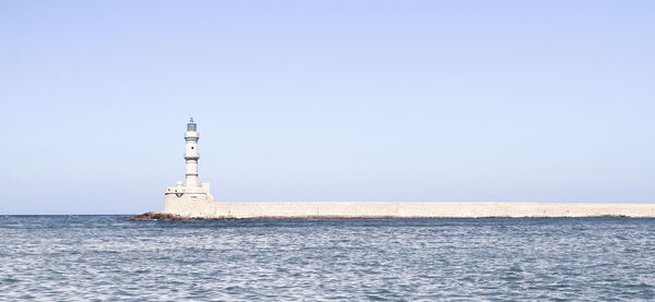 Lighthouse by sea against clear sky