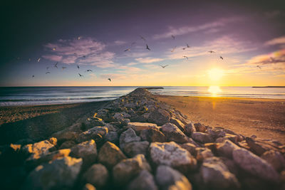 Pier at beach against sky during sunset