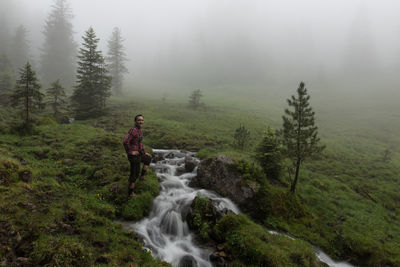 Man standing by stream on field during foggy weather