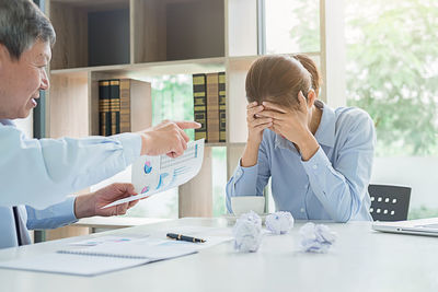 Businessman holding document while talking to stressed colleague in office